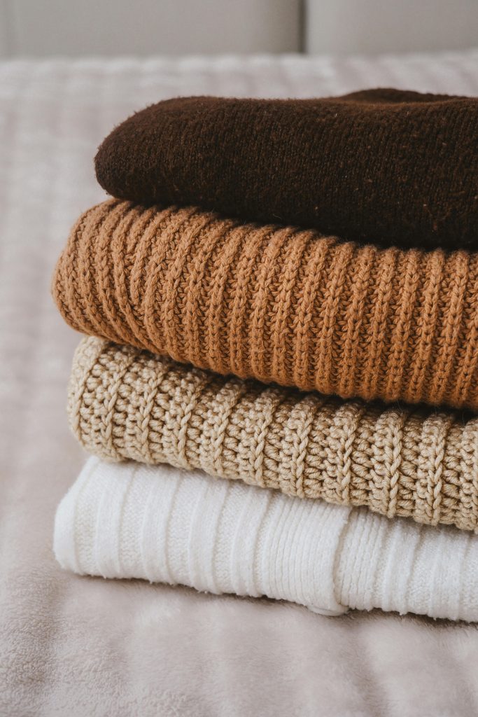 A stack of warm knitted sweaters in earthy tones, perfect for cozy winter days.