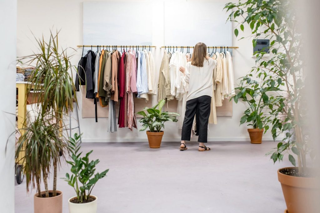 Woman browsing clothes in a boutique surrounded by indoor plants and stylish displays. Ideal fashion retail scene.