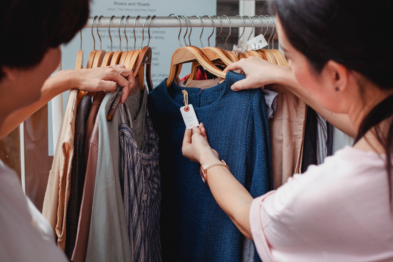 Two women browse clothes in a boutique, examining a blue dress.