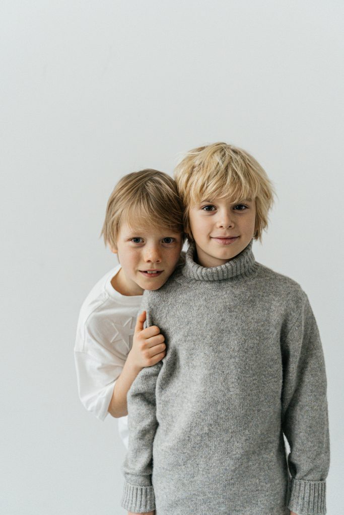 Charming portrait of two smiling boys wearing cozy sweaters against a soft white background.